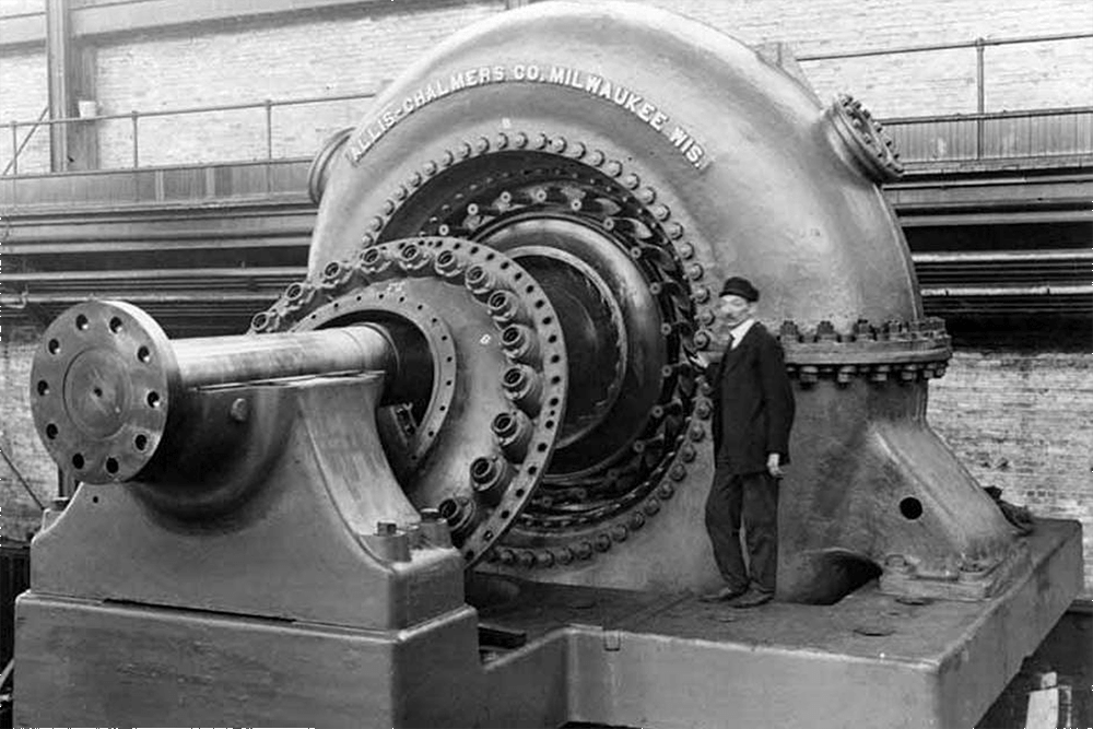 Man standing near Allis-Chalmers generator unit, unidentified powerhouse, n.d.